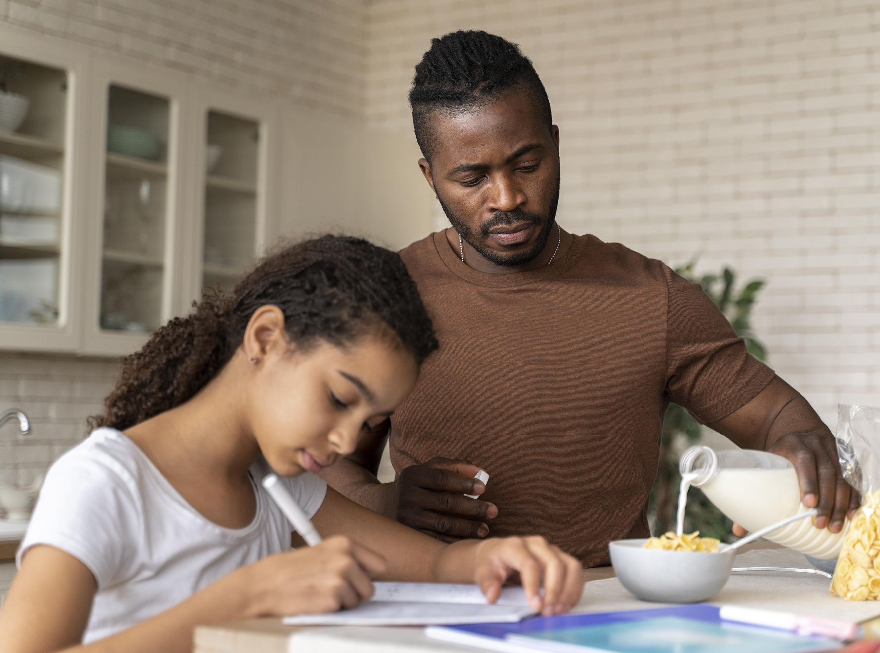 Black father helping daughter with schoolwork at the kitchen table.